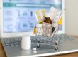 Shopping cart toy with medicines in front of laptop screen with pharmacy web site on it. Pills, blister packs, medical bottles, thermometer set. Health care and buying medications online.