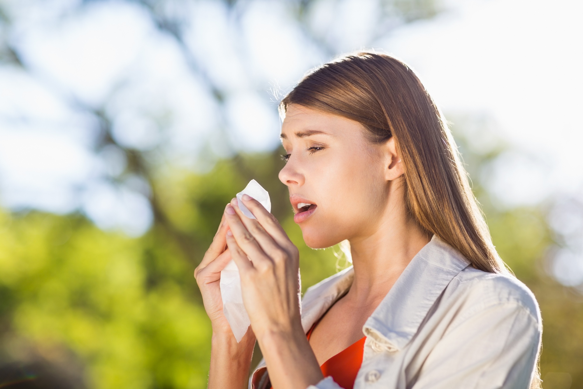 A woman with pollen allergies, sneezing into a tissue.