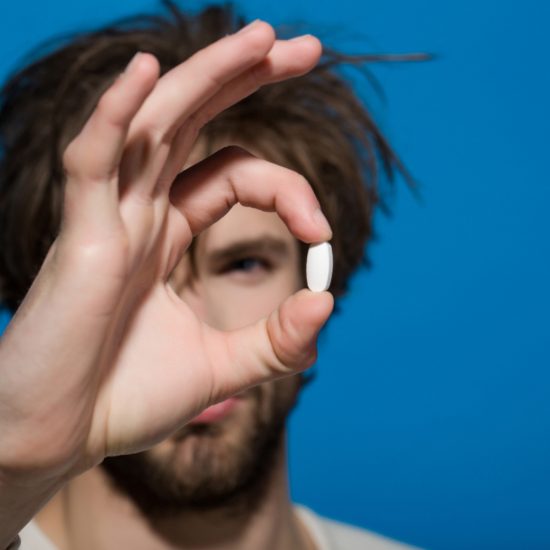 Man holding a white pill in his hand. Pill is in focus against a bright blue background, showing the importance of Zoloft for people with depression.
