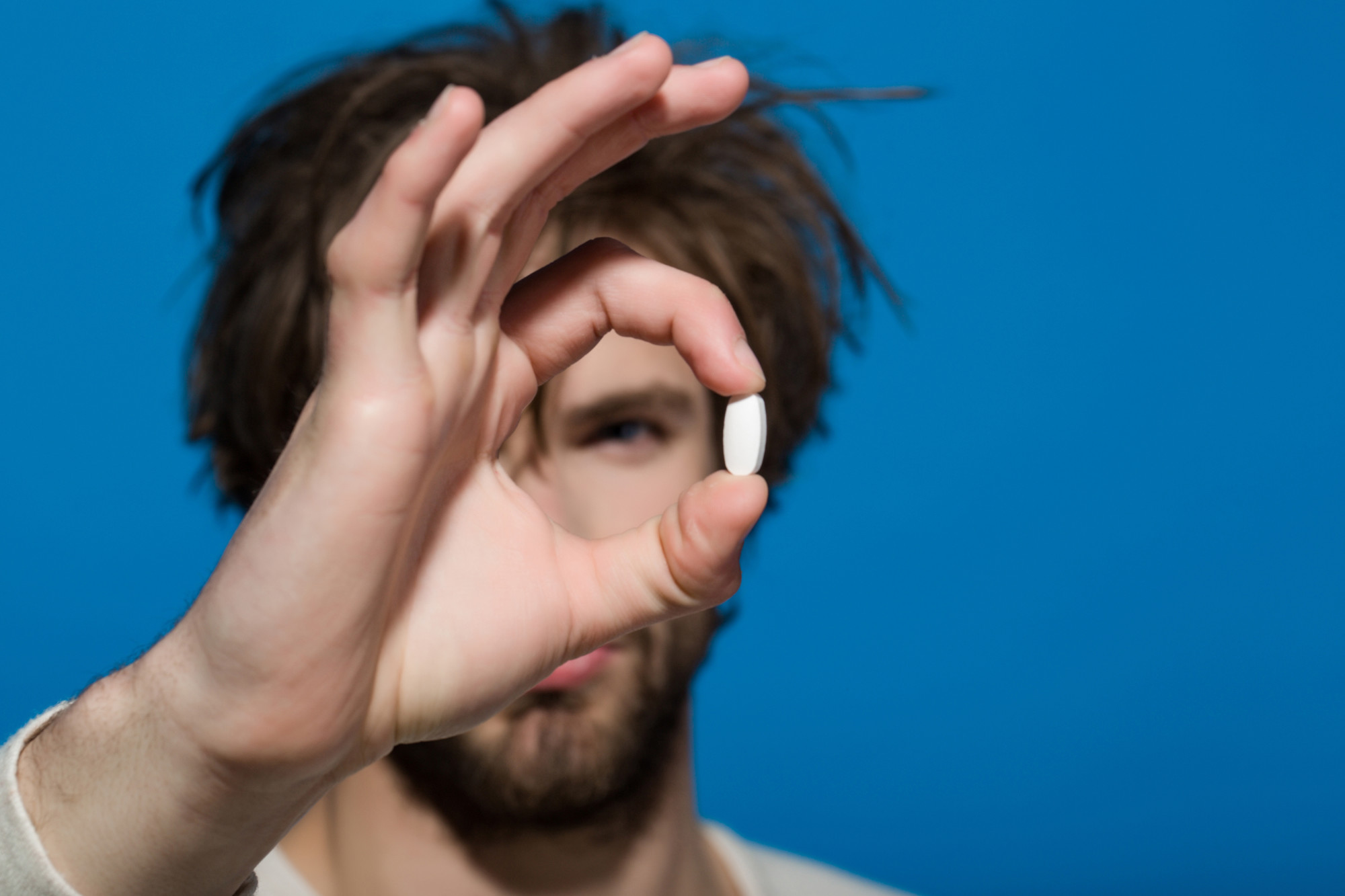 Man holding a white pill in his hand. Pill is in focus against a bright blue background, showing the importance of Zoloft for people with depression.