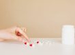 Hand choosng between a few pills that are strewn out on a table, indicating having to ration medications due to limited/low supplies..