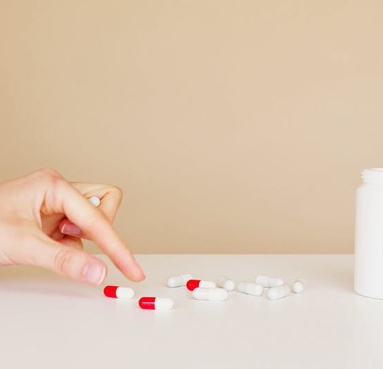 Hand choosng between a few pills that are strewn out on a table, indicating having to ration medications due to limited/low supplies..