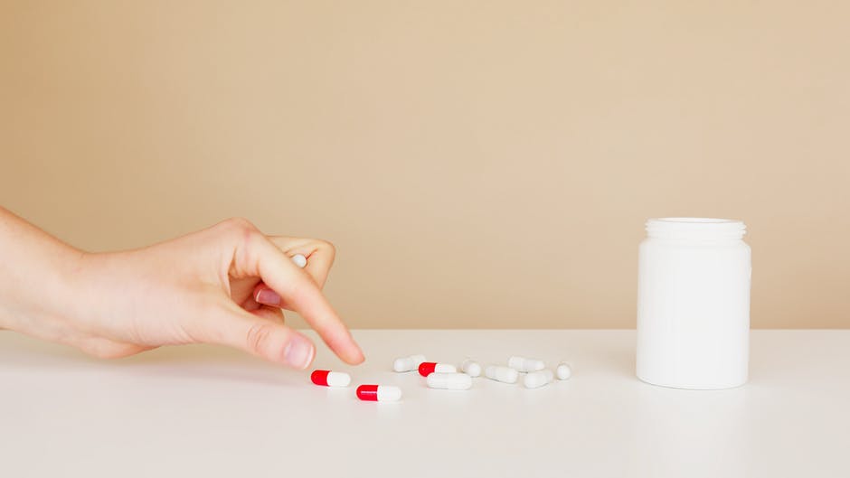 Hand choosng between a few pills that are strewn out on a table, indicating having to ration medications due to limited/low supplies..