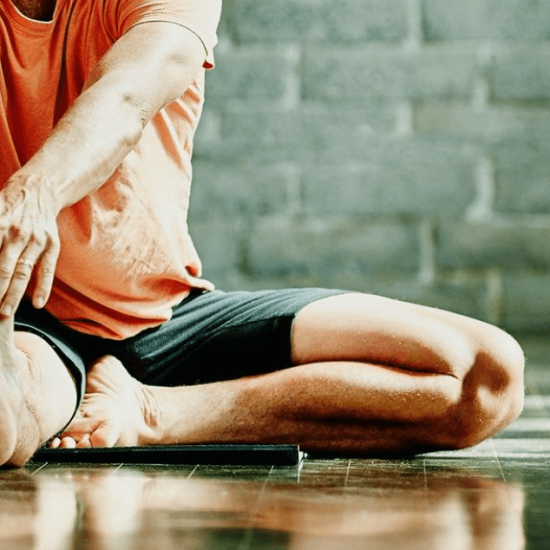 Man seated on floor stretched out right leg to exercise and strengthen ahead of knee surgery