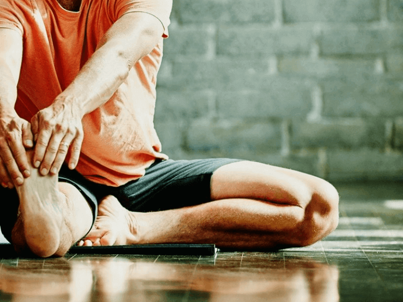 Man seated on floor stretched out right leg to exercise and strengthen ahead of knee surgery